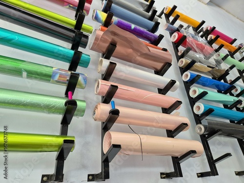 Colorful cutting sticker rolls of vinyl film stored on black wall racks in a workshop or print studio