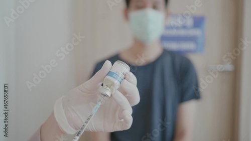 A man is holding a vaccine bottle and wearing a mask. The bottle is labeled with the word 