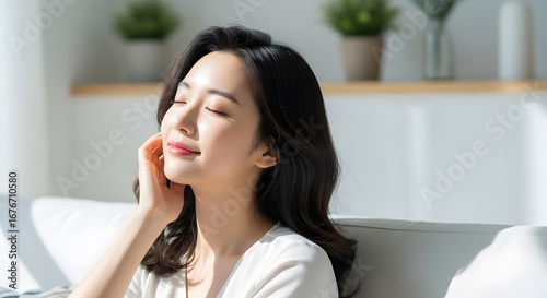 Portrait of a serene young Asian woman relaxing on a comfortable sofa, enjoying a peaceful and cozy weekend morning at home with beautiful natural sunlight. Free Download Portrait of a serene young Asian woman relaxing on a comfortable sofa, enjoying a peaceful and cozy weekend morning at home with beautiful natural sunlight. - GFXLoad