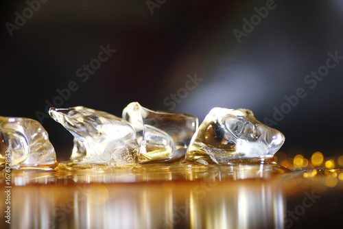 Close up of melting ice on golden liquid surface