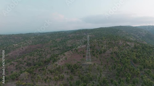 Aerial View of a Power Transmission Tower Surrounded by Lush Greenery and Rolling Hills