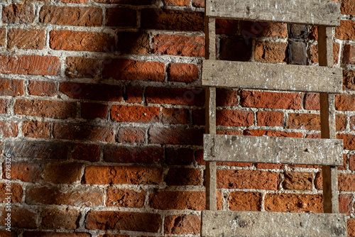 old imperial red brick wall and a ladder leaning against the wall casting a shadow