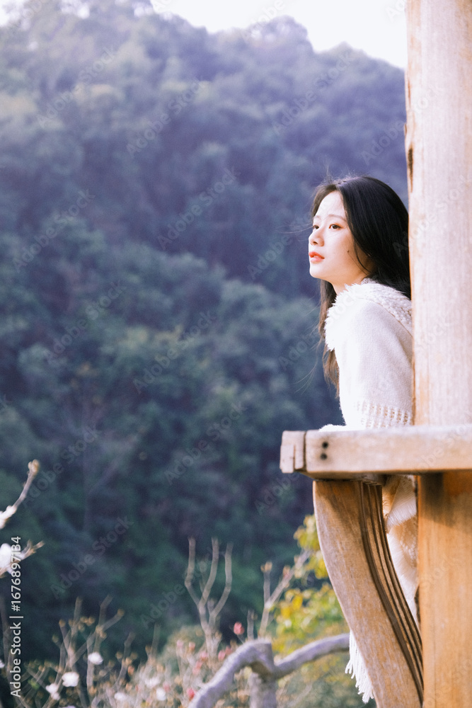 Naklejka premium A woman in a cozy white sweater gazes thoughtfully into the distance in a serene outdoor setting.