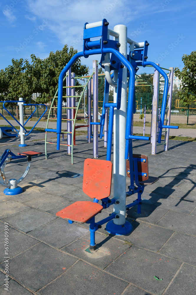 Fototapeta premium outdoor gym equipment with seats and metal handles installed on public sports ground, fitness machine for street workout and physical activity
