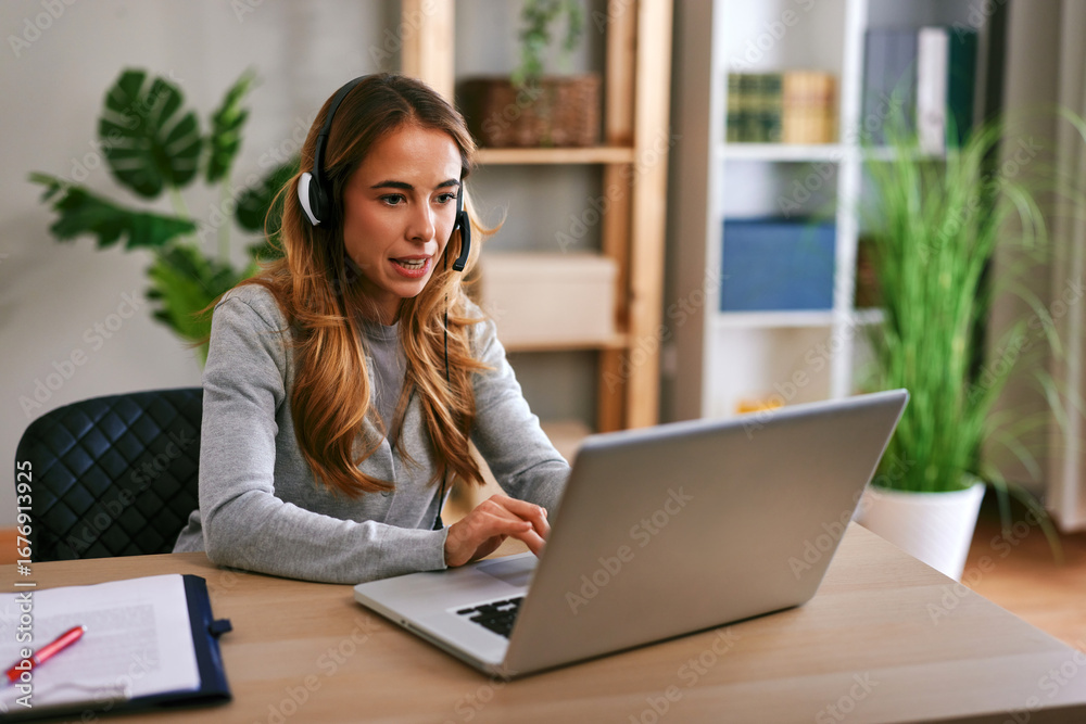 Young woman working from home office using laptop and headset Young woman working from home office using laptop and headset