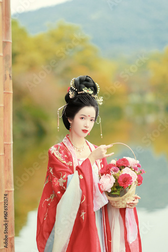 Elegant woman in traditional hanfu holding a flower basket by the water.