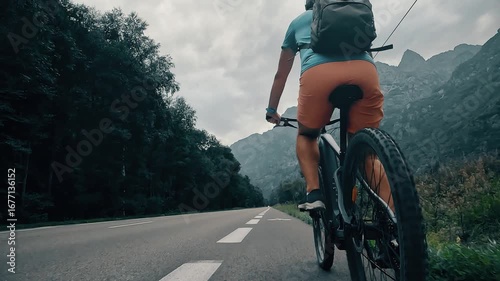 Rear view of a cyclist riding on a road in the French Alps, camera following behind the rider. Scenic mountain landscape
