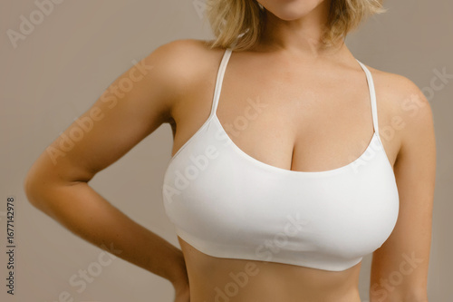 Close-up of a woman's chest in a white sports bra, showing natural breast shape. Concept of plastic surgery, beauty care, breast health, and body aesthetics.