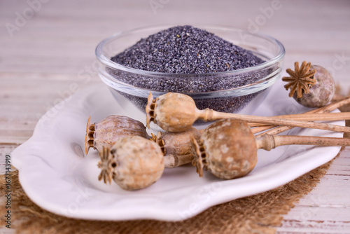 Poppy seeds in a transparent bowl and dried poppy heads, on a white background.	