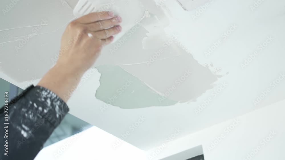 Worker's hand applying putty on ceiling during interior renovation ...