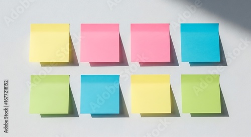 Eight colorful sticky notes in various shades of yellow, pink, blue, and green arranged on a light background with shadows.
