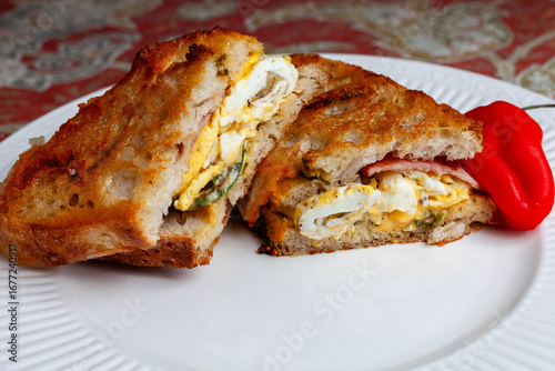 A savory breakfast grilled cheese sandwich with Canadian bacon, fried eggs, American cheese, sauteed jalapenos on grilled cheddar-jalapeno sour dough bread.