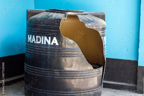 Damaged black plastic water tank with a large hole in the side