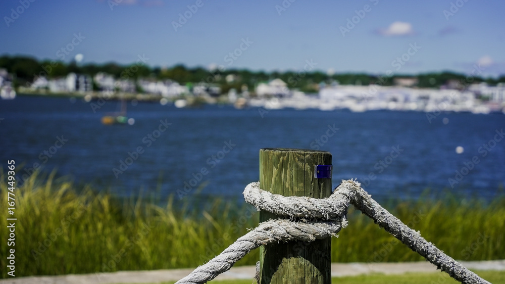 Obraz premium Rope tied to a wooden post with a tranquil waterfront view during a sunny day