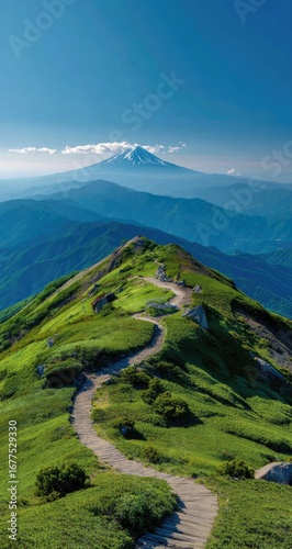 Winding mountain trail ascends a verdant ridge, leading towards a majestic snow-capped peak under a clear, vibrant blue sky