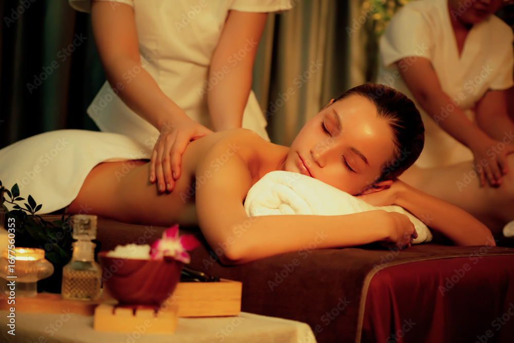 Fototapeta premium Caucasian couple customer enjoying relaxing anti-stress spa massage and pampering with beauty skin recreation leisure in warm candle lighting ambient salon spa at luxury resort or hotel. Quiescent