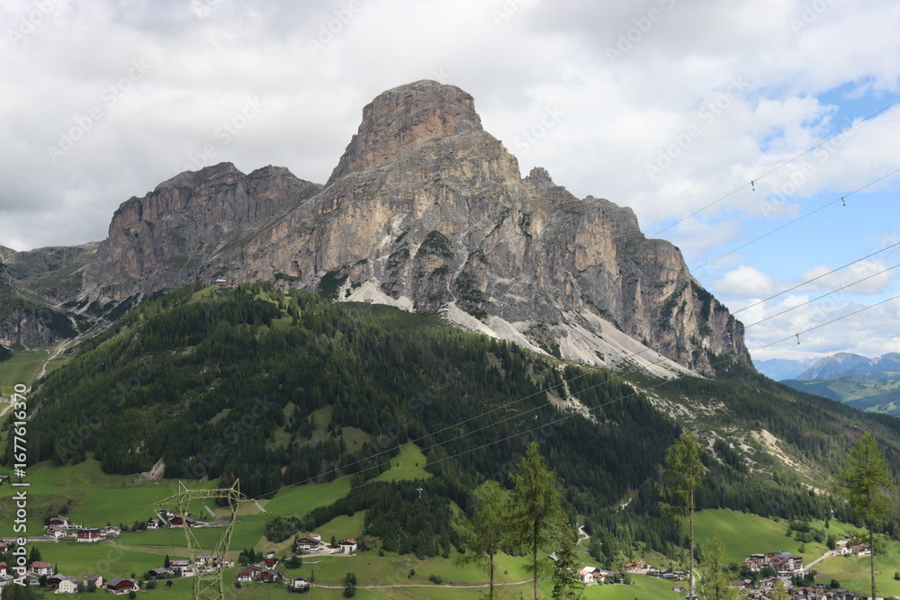 Naklejka premium Trentino, Italy - July 29, 2025: Panoramic view of the majestic Piz Boe and the surrounding Dolomite peaks, with lush green valleys and scattered snow, under a clear blue sky. beautiful view to Lake b