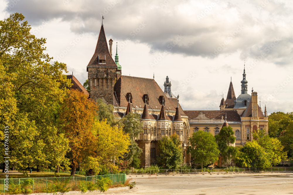 Fototapeta premium Vajdahunyad Castle in City Park showcasing eclectic architecture with Romanesque, Gothic, Renaissance, and Baroque styles, surrounded by golden autumn foliage. Budapest, Hungary.