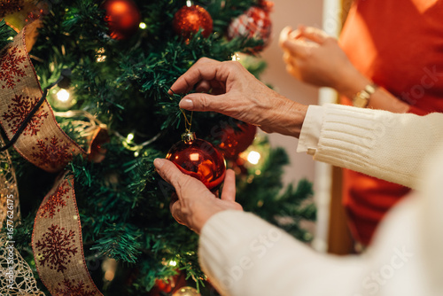 Grandmother hanging christmas ball ornament on christmas tree with family