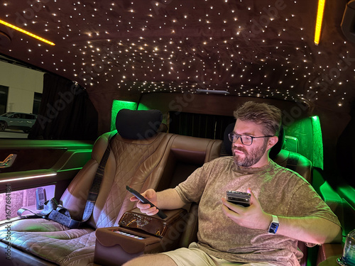 Man focused on smartphone inside luxury illuminated vehicle. Concentration, technology and modern lifestyle in travel environment.