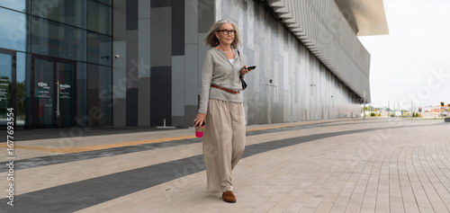 фотографія Mature woman walking confidently on modern plaza in urban setting during daytime