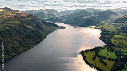 aerial drone shot flying down ullswater lake in mountain hill valley with mountains in background at sunset in summer in England lake district