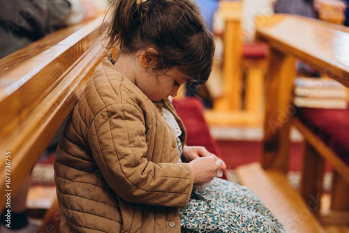 30.01.25 Vinnitsa, Ukraine: A little girl sits on a bench in a church during a service, spinning and looking around, sometimes bored