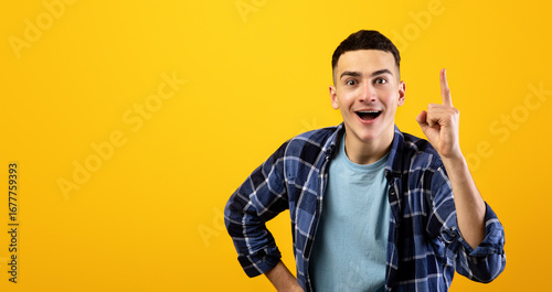 Canvas Print Handsome young guy in casual clothes pointing upwards on orange studio background