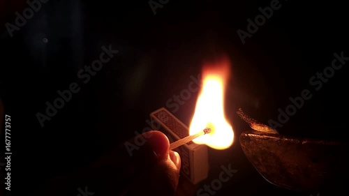 Slow-motion horizontal shot from India, a hand delicately lights a diya against a black background, capturing the essence of spiritual preparation and the vibrant warmth of Diwali festival celebration