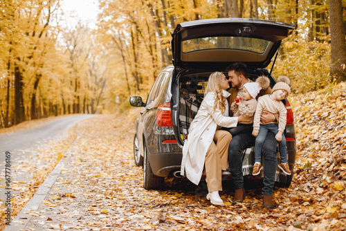 Young family sitting at open trunk of hatchback car in autumn forest