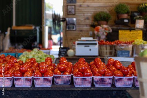 Fresh red tomatoes in white baskets displayed on a market stall. In the background, more fruits and vegetables can be seen along with a rustic wooden stall.Concept of healthy food, farming, and local 