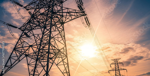 Electrical transmission towers against a bright cloudy sky with sunlight shining through.