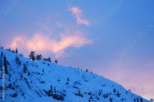 The sunset light hits a wispy cloud over a snow covered mountain