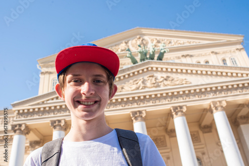 Portrait of a teenager in a red cap, a child in a white T-shirt with a backpack stands in front of the Bolshoi Theater - a landmark of Moscow.