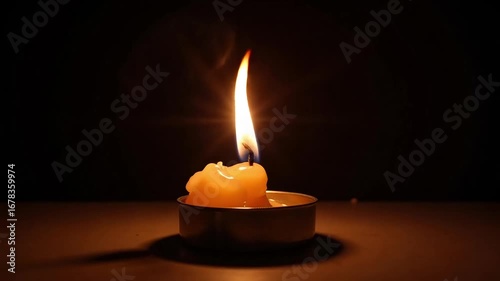 A lone candle flame burns brightly in the dark, casting a warm glow.
