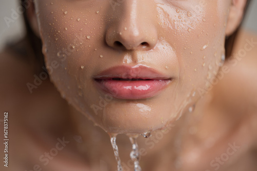 A young woman with fresh, clean skin smiles in the shower as water splashes on her face