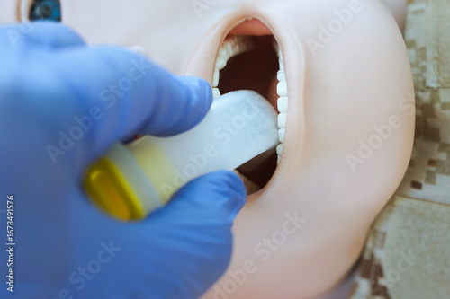A gloved hand inserting an oropharyngeal airway tube into a medical training mannequin in camouflage uniform for airway management practice. Correct demonstration of airway tube placement during tccc.