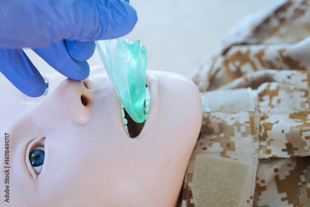 Fototapeta premium Medical training mannequin in camouflage uniform during insertion of an i-gel supraglottic airway device. The procedure illustrates airway management placement as part of a military medical simulation