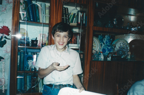 Twelve-year-old boy laughs in surprise looking at camera, photo taken with flash in home interior, captured in analog photography style from mid-1990s Ukraine
