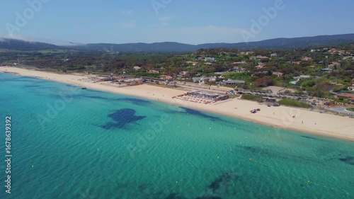 aerial footage showcasing the pristine turquoise waters and golden sands of Pampelonne Beach in Ramatuelle, near Saint Tropez on the French Riviera, with lush coastal vegetation and scattered villas i