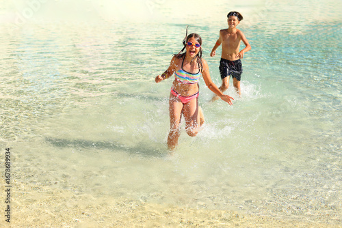 children joyfully playing in the water at the beach. With the sun shining and waves gently lapping at the shore, their laughter fills the air as they splash and play together