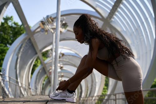 Young sporty woman tying shoelaces on modern bridge