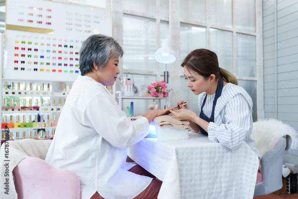 Obraz premium Senior asian woman receiving manicure treatment from young nail spa technician in small salon promoting beauty grooming personal care wellness hygiene relaxation lifestyle professional environment