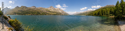Panoramic view of Lake Sils and the village of Isola, with the surrounding mountains, in summer.
