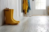 Waterproof vinyl planks flooring concept. Yellow rain boots placed by a door on a wet floor, suggesting a rainy day indoors.