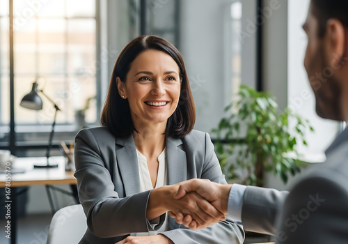 Smiling businesswoman shaking hands, successful business meeting, modern office, partnership, agreement, confident, professional, collaboration.