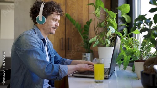 Young man wearing headphones sitting at a desk in front of a laptop, focused and engaged, possibly working, studying, video calling, or gaming.