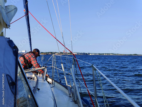 Sailman is preparing boat for docking, view from the deck of a sailing yacht towards the horizon with a distant city Hanko. Nautical adventure, travel, and connection between sea and urban landscape
