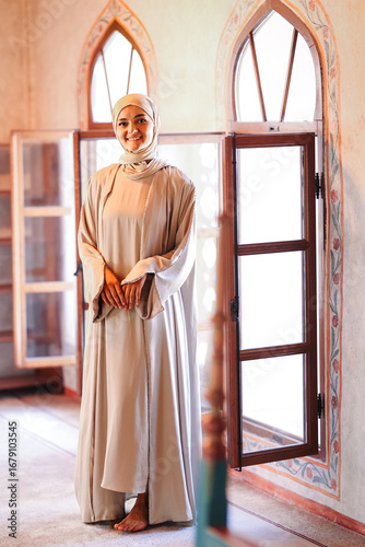 Принти на полотні Smiling Muslim woman in traditional clothing standing barefoot inside a mosque,