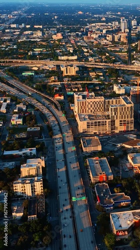 Facades of multiple houses are lit with sun at sunset. Numerous cars move by the highways of Miami, Florida, USA. Vertical video